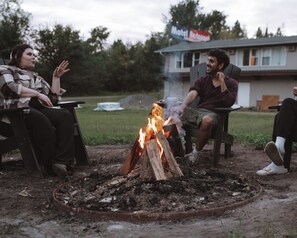 Un groupe de personnes assises autour d’un feu de camp, dans un cadre extérieur.