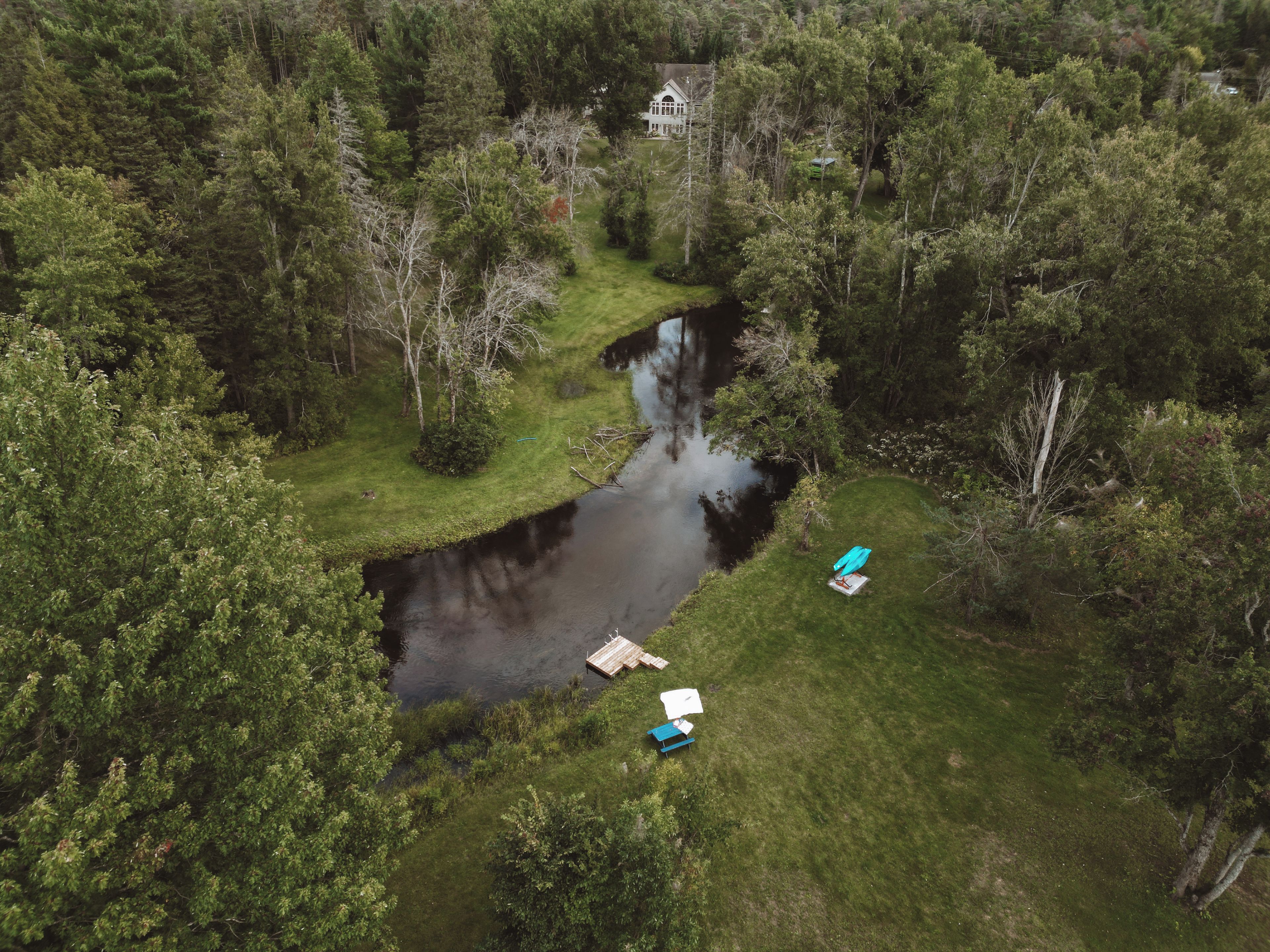 An aerial view of a property with a river, surrounded by dense forest, and a house in the background.