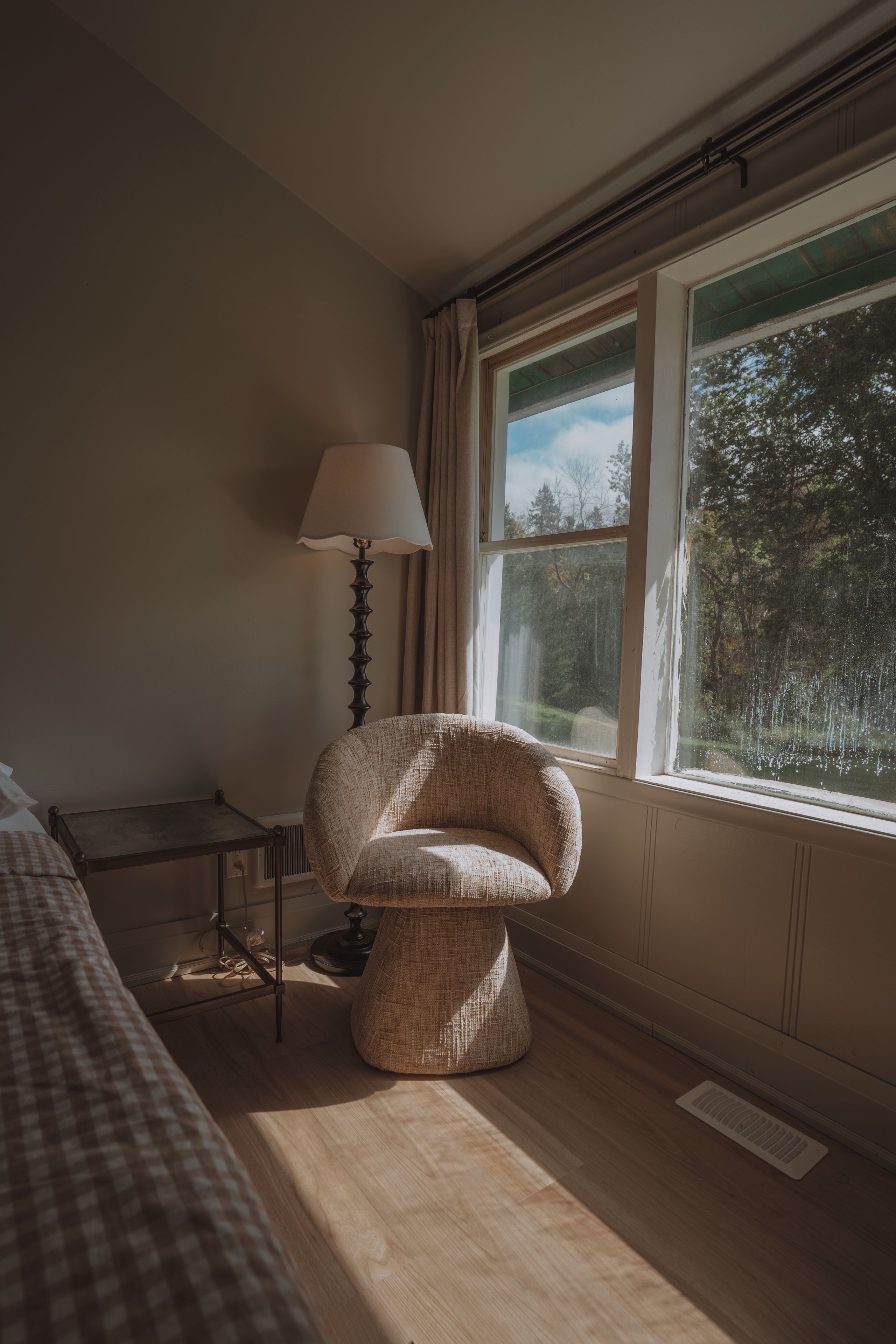 A room with a chair near a window, a lamp, and a bed with checkered bedding.