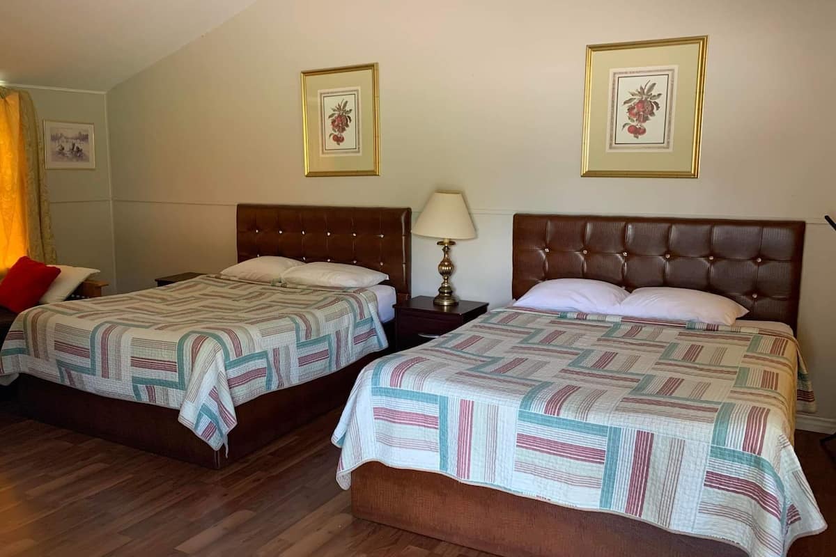 Habitación de hotel con dos camas, suelo de madera y dos cuadros con flores en la pared.