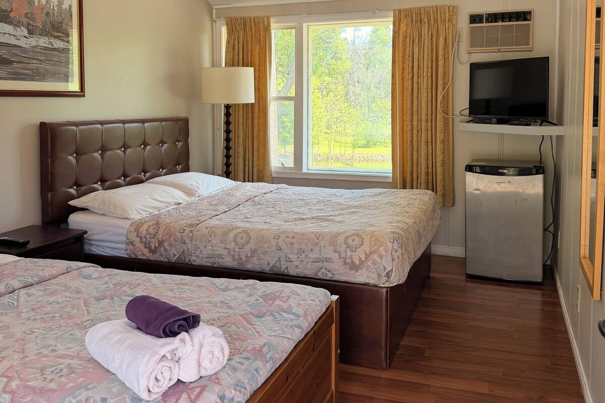 Habitación de hotel con dos camas, televisión, refrigerador y ventana con cortinas.