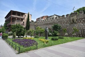 A historic building with a balcony, a statue, and a stone wall. - Emily guest house (T'bilisi)