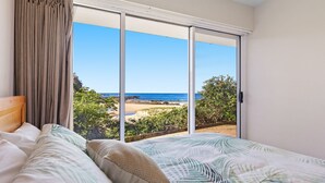 A bedroom with a bed, a view of the beach, and a sliding glass door. - Malua Dream on Kuppa Avenue (MALUA BAY)
