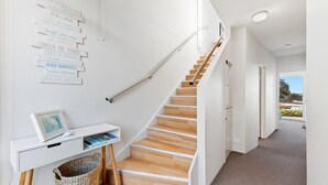 A modern interior with a wooden staircase, a white desk with a picture frame and books, and a wall with motivational quotes. - Malua Dream on Kuppa Avenue (MALUA BAY)