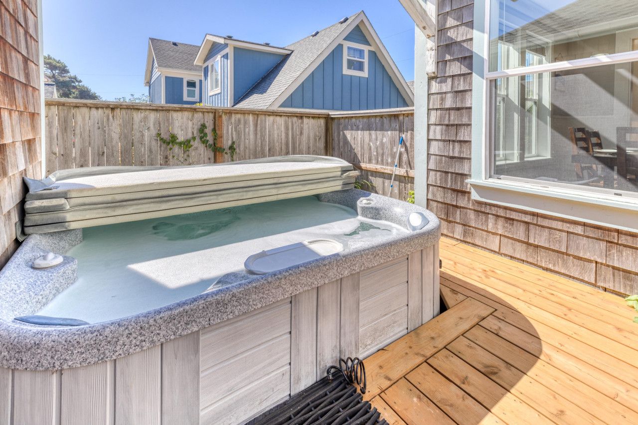 A hot tub in a backyard with a wooden deck and a house in the background.