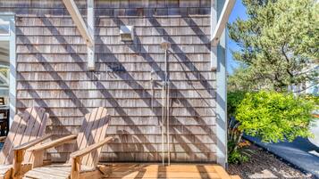 A wooden deck with Adirondack chairs, a metal showerhead, and a wooden wall with shingles.