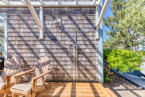 Une terrasse en bois avec des fauteuils Adirondack, une pomme de douche en métal et un mur en bois recouvert de bardeaux.