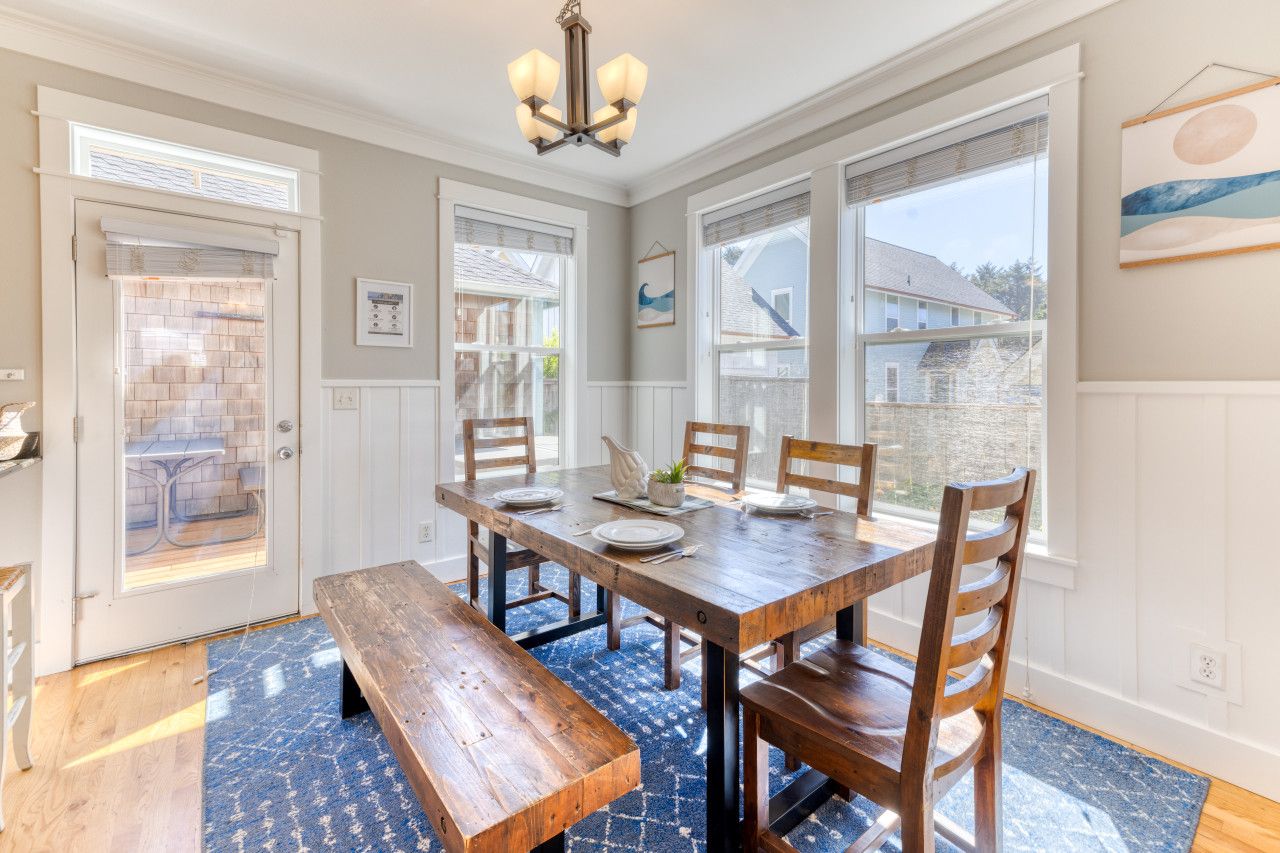 A dining area with a wooden table set for four, benches, and a view of the outside through large windows.