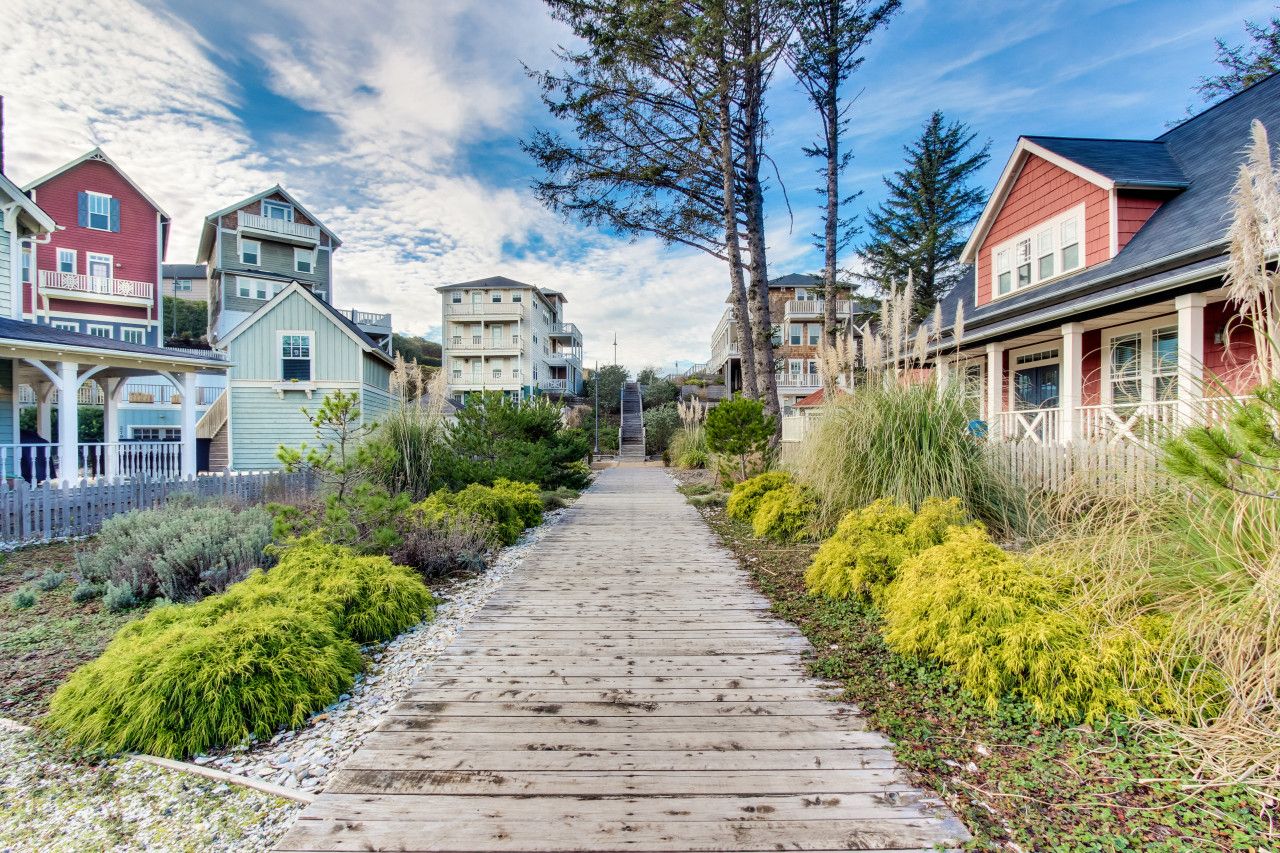 A wooden pathway leading to a row of colorful houses with balconies, surrounded by lush greenery.