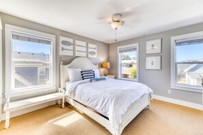 Une chambre à coucher avec un lit, un banc, un ventilateur de plafond et des tableaux encadrés accrochés au mur.