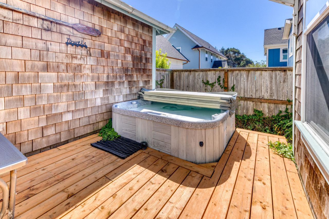 A hot tub in a backyard with a wooden deck and a fence.