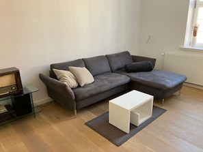 Ein modernes Wohnzimmer mit einem grauen Ecksofa, einem weißen Couchtisch und einer TV-Konsole aus Glas.