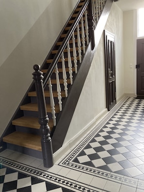 Eine Treppe mit Holzstufen und schwarzen Spindeln, die zu einer Tür mit einem geometrisch gemusterten Boden führt.