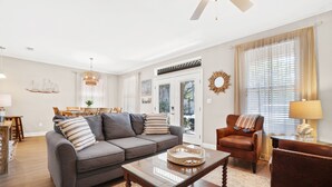 A living room with a gray sofa, a wooden coffee table, and a brown armchair. There is a dining area with a table and chairs in the background. - KonoVilla * Dog Friendly * Best Lagoon Pool in Destin (Destin)
