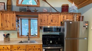 A kitchen with wooden cabinets, a stainless steel refrigerator, a stove, and a microwave. - Maggies on the Bayou, close to Hiking, Beaches, Boating, Golf (Ludington)