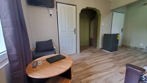 A room with a round wooden table, a black chair, a flat-screen TV mounted on the wall, and a door leading to another room.