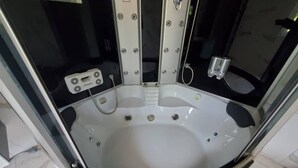 A modern, enclosed hot tub with a control panel, built-in seating, and a glass enclosure.