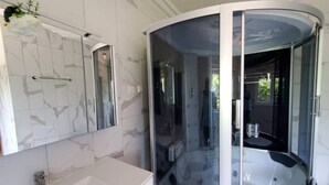 A modern bathroom with a curved glass-enclosed shower, a white marble-tiled wall, and a large mirror above the sink.
