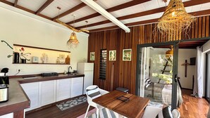 Una cocina moderna con detalles de madera, un comedor con mesa de madera y sillas blancas, y un amplio ventanal con vistas al exterior.