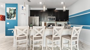 A modern kitchen with dark cabinets, a white island with bar stools, and pendant lighting. - Sunnyside Cliffs | Near Attractions | Private Pool (Davenport)