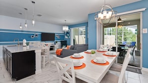 A modern kitchen with a dining area, featuring a large island, white cabinetry, and a blue accent wall. - Sunnyside Cliffs | Near Attractions | Private Pool (Davenport)