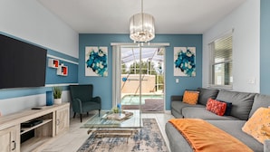 A living room with a glass coffee table, a grey sofa, and a blue accent wall. - Sunnyside Cliffs | Near Attractions | Private Pool (Davenport)