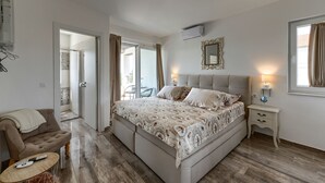 Ein Schlafzimmer mit einem großen Bett, einem Nachttisch, einem Sessel und einer Tür zu einem weiteren Raum.