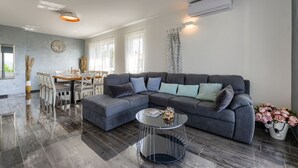 Ein modernes Wohnzimmer mit einem Ecksofa, einem runden Couchtisch und einem Essbereich mit Tisch und Stühlen.