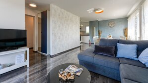 Ein modernes Wohnzimmer mit einem Flachbildfernseher, einem dunklen Sofa und einem Couchtisch.