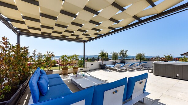 Eine Dachterrasse mit blauer und weißer Außenbestuhlung, Topfpflanzen und Blick auf die Landschaft.