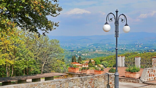 Un mur de pierre avec une rambarde métallique, un lampadaire et des plantes en pot.