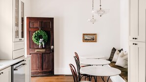A kitchen with white cabinets, a wooden door, a chandelier, and a dining area with a round table and chairs. - Designer Retreat in Quaint Historic District w Front Porch Dining under the oaks (Greenville)