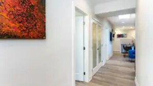 Een gang met een houten vloer, witte muren en een schilderij aan de linkerkant.