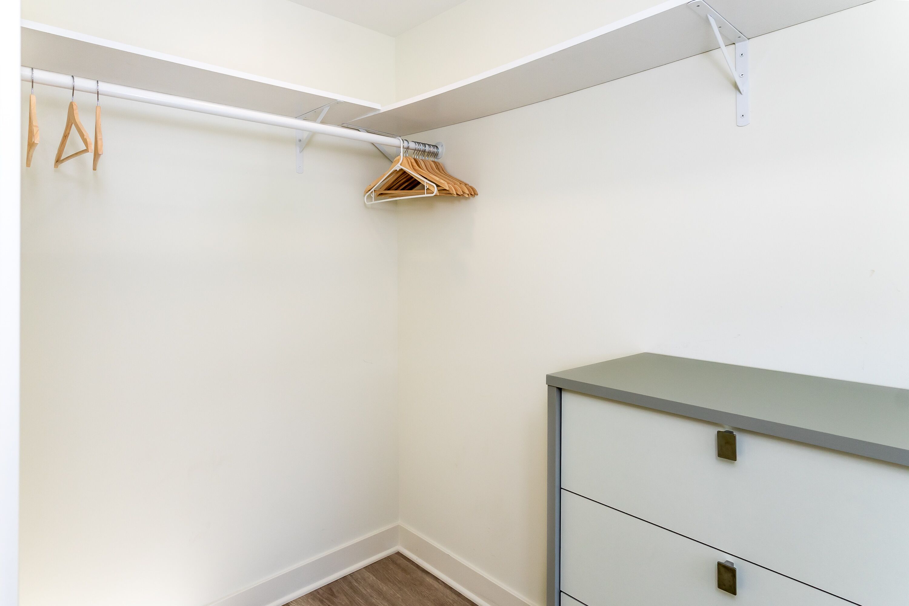 A corner of a room with a white wall, a wooden hanger rack, and a grey cabinet with drawers.