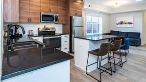 Een moderne keuken met houten kastjes, roestvrijstalen apparatuur, een zwart aanrecht en een bar met krukken.