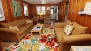 A wooden-paneled living room with two sofas, a coffee table, and a floral rug. - "The Hammock Cottage" (Kill Devil Hills)