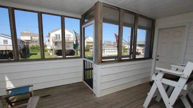 A covered porch with wooden flooring, white railings, and large windows offering views of neighboring houses. - "The Hammock Cottage" (Kill Devil Hills)