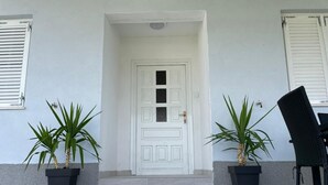 A white door with a small porch area, flanked by two potted plants and a chair. - Click Here - Get Promo Price By Inquiry - Apartments Nenna With 3 Bedrooms (Mravince)