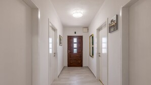 A hallway with white walls, a wooden door at the end, and a ceiling light. - Click Here - Get Promo Price By Inquiry - Apartments Nenna With 3 Bedrooms (Mravince)
