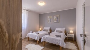 A bedroom with two beds, a white rug, a wooden floor, and a ceiling light. - Click Here - Get Promo Price By Inquiry - Apartments Nenna With 3 Bedrooms (Mravince)