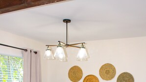 A round wooden dining table with four chairs, a hanging light fixture, and four woven placemats on the wall.