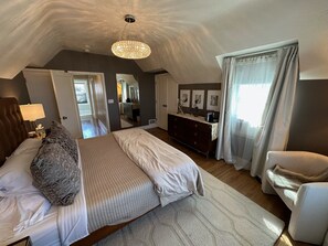 Um quarto com uma cama grande, cômoda, cadeira, espelho e lustre.