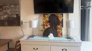 A living room with a flat-screen TV mounted on the wall, a white cabinet with drawers, a chair, and a rug on the floor.