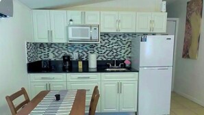 A compact kitchen with white cabinets, a microwave, a refrigerator, and a dining table with chairs.