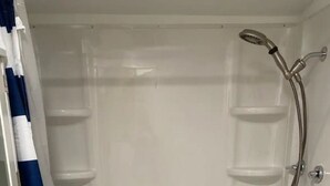 A white shower enclosure with a handheld showerhead and a built-in shelf.