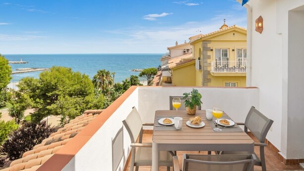 A balcony with a table set for breakfast overlooking a coastal view.
