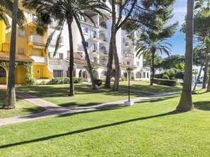 A well-maintained courtyard with a pathway, palm trees, and a building with balconies. - Penthouse in Andalucia del Mar for 2 people | ADM 4-504 (Puerto Banús - Marbella)