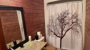 A bathroom with wooden walls, a sink, a toilet, and a shower curtain with a tree design.