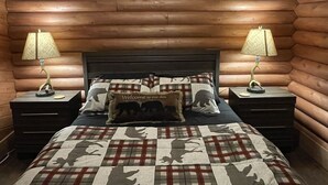A log cabin-style bedroom with a bed, two nightstands, and a welcome pillow.