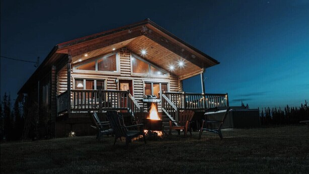 A log cabin with a porch, outdoor seating, and a fire pit.